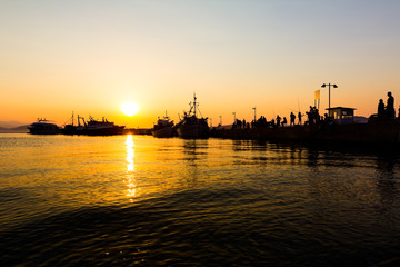 Fototapeta premium Silhouetted shot of a people fishing on pier at sunset