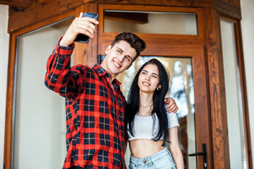 Happy romantic couple taking a photo with smart phone. Beautiful young girl and man hug and laugh taking a selfie. Urban fashion style