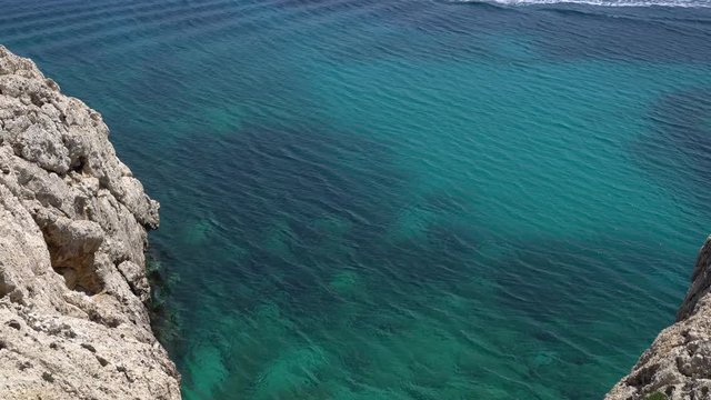 White motor boat floats in calm turquoise sea waters. Watching rom the rocky cliff over transparent wvaes. Handheld shot