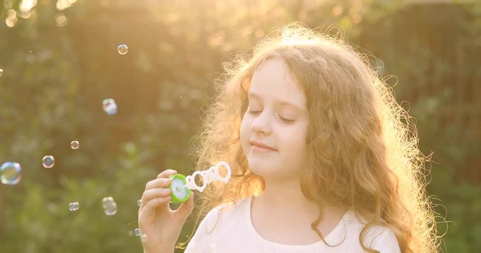 Curly haired girl blowing soap bubbles in sunset.