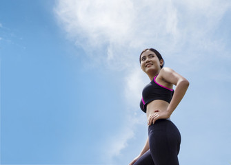Young happy sportswoman in sportswear looking away and standing against blue sky background. Healthy lifestyle and sport activity concepts. Copy space.