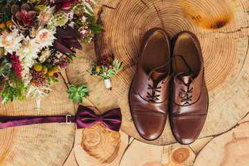 Close up of modern man accessories. purple bow-tie, leather shoes, belt and flower boutonniere on wood chair rustic.