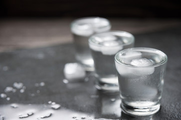 Vodka shots with ice cubes on black stone,
