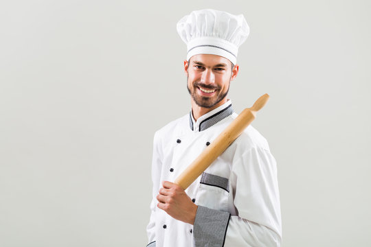 Portrait of chef holding rolling pin on gray background.