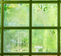 Green window with condensation, high humidity. Texture of water on a glass. Blur garden background. Phenomenon of nature concept.