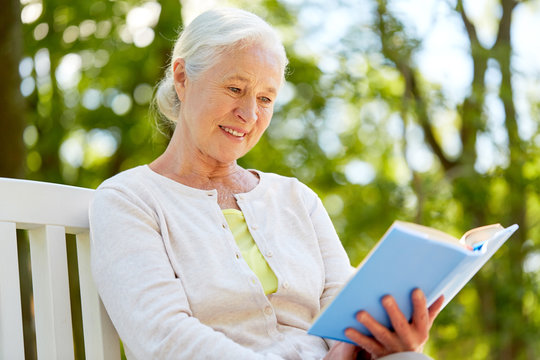 happy senior woman reading book at summer park