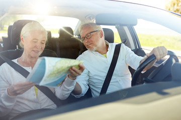 happy senior couple with map driving in car