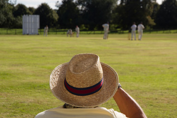 Spectator wearing sunhat watching cricket match on English village green