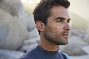 Fototapeta premium Good looking guy in wetsuit on beach, looking away