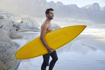 Shirtless surfer dude on beach holding board