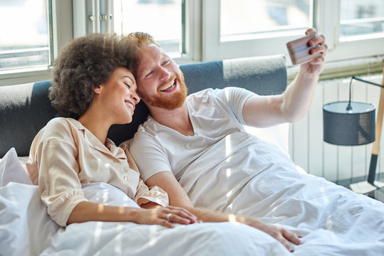 Young couple making selfie while lying in bed