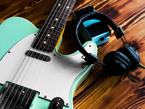 Electric guitar, pedal and headphones on vintage wooden table. Close up.