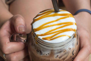 Woman handle a glass of iced chocolate whith caramel.
