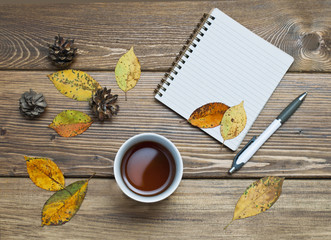 Naklejka na ściany i meble Cup of tea and a notebook on a wooden table, yellow leaves concept of autumn, mood and coziness.