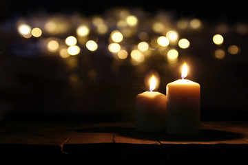 Fototapeta premium Burning candles over old wooden table with bokeh lights