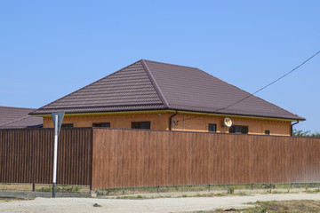 A house with a metal corrugated roof and a gauve fence made from a brown metal profile