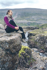 Naklejka premium Girl in warm clothing sits on the cliff on background of mountains of Iceland.