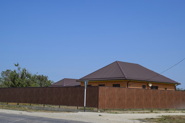 A house with a metal corrugated roof and a gauve fence made from a brown metal profile