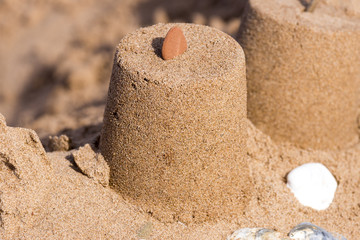 Fototapeta na wymiar Sand castle pillar with red stone on top, seashells at base