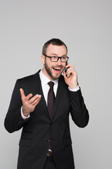 Half-length shot of cheerful young businessman in a suit talking on the phone and throwing his hand up