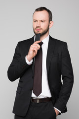 Half-length shot of young businessman in a suit holding his smartphone to his chin with a pensive look on his face