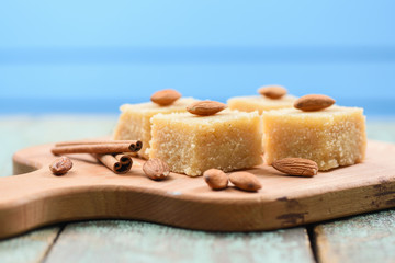 Traditional Indian sweetmeats, semolina halava with almonds on wooden board copyspace