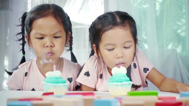 Two asian little girl blows out candles on birthday cake together in house. Slow motion shot in studio.