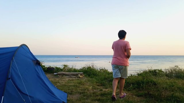 Woman approaches a cliff near the sea shore and takes pictures.