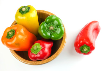 Red yellow and green bell pepper in a wooden bowl over white