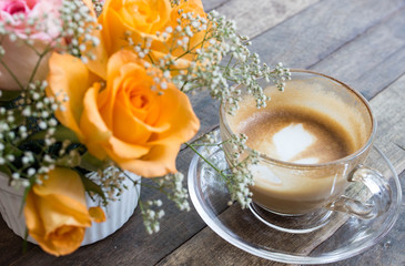 Half cup of coffee on wooden desk with blurred orange color roses beside , soft focus