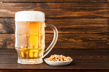 glass of cold frothy lager beer and snacks on wooden table