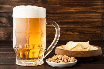 glass of cold frothy lager beer and snacks on wooden table