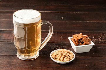 glass of cold frothy lager beer and peanuts plate on wooden table
