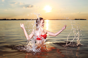 Красивая девушка плескается в воде на закате солнца