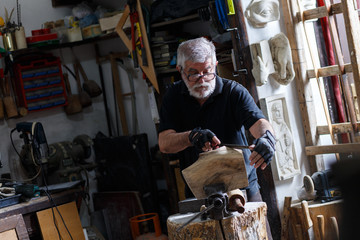 Fototapeta na wymiar Senior sculptor working on his sculpture in his workshop.
