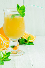 Orange juice in a glass on a white wooden table with whole and sliced ​​oranges