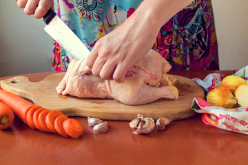 Woman chopping raw chicken for cooking in kitchen