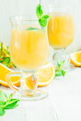Orange juice in a glass on a white wooden table with whole and sliced ​​oranges