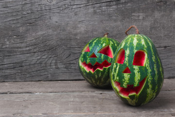 Watermelon with a smiling face like a pumpkin for Halloween. Wooden table and old boards. Empty space for text.