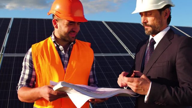 Close up view of business client talking to engineer at solar energy station. Solar panels in the field, client and worker discussing setup of solar panels.