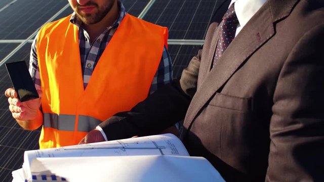 Alternative energy station concept, iew of worker and businessman discussing project, solar panels behind them.