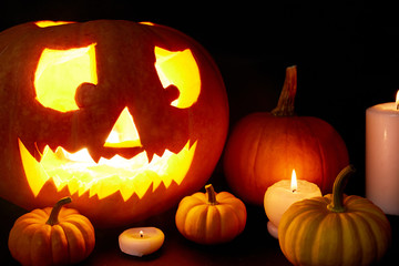 Fototapeta premium Ripe pumpkins surrounded by burning candles and carved jack-o-lantern