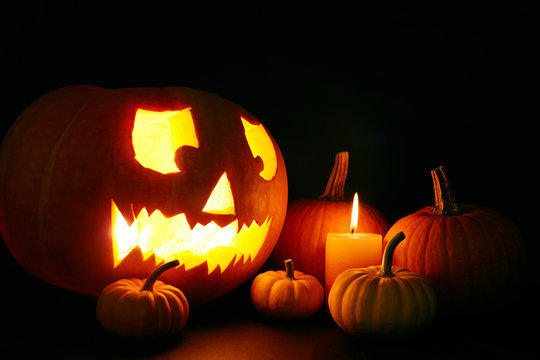 Jack-o-lantern, burning candle and several ripe pumpkins in the dark