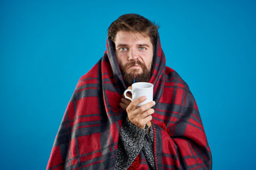 A man with a beard on a blue background in a plaid holds a mug, sickness, sick, flu