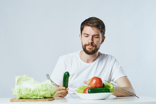 Man with a beard on a light background holds vegetables at a table, diet, vegetarian