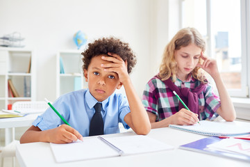 Tired schoolboy and his classmate drawing in copybooks