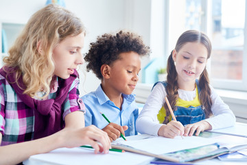 Friendly pupils with pencils drawing picture together in copybook at lesson
