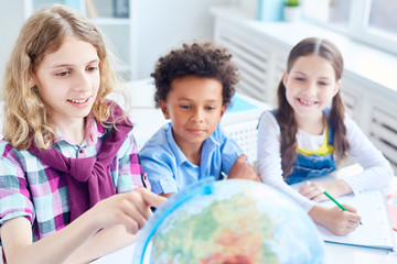 Fototapeta premium Little school friends discussing territory on globe model at geography lesson
