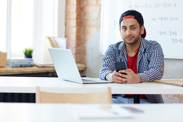 Guy in casualwear sitting by workplace in classroom of college