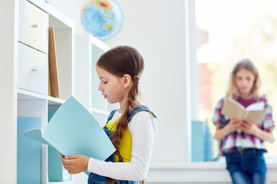 Schoolgirl choosing book in library for lesson of literature